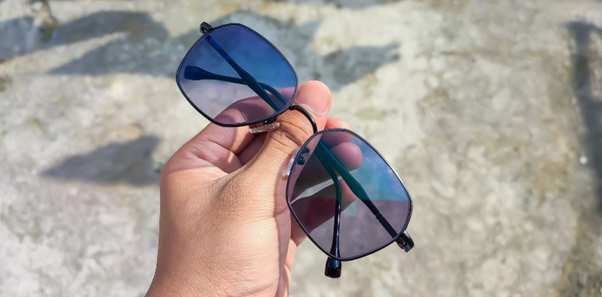Hand holding a pair of photochromic sunglasses outdoors