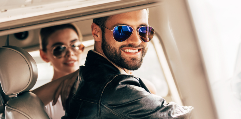 A man in an aeroplane wearing aviator style sunglasses and a leather jacket.