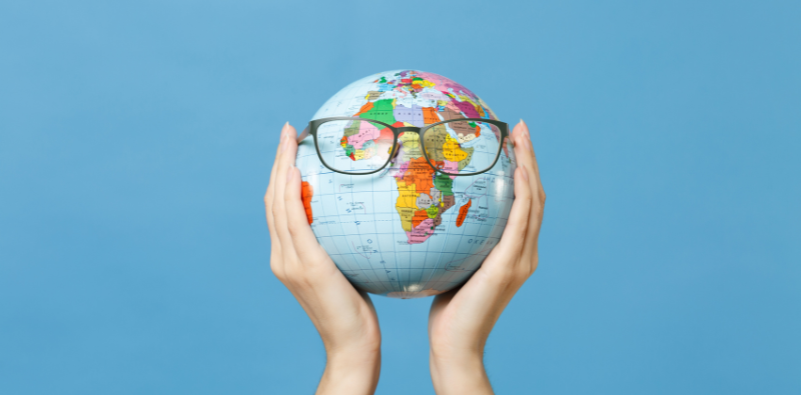 A globe with a pair of glasses on it, held up in the air against a blue background.