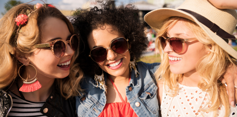 Three young women wearing sunglasses and smiling.