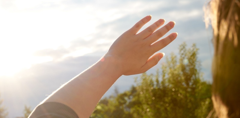 A person outside, holding up their hand to shield their eyes from sunlight