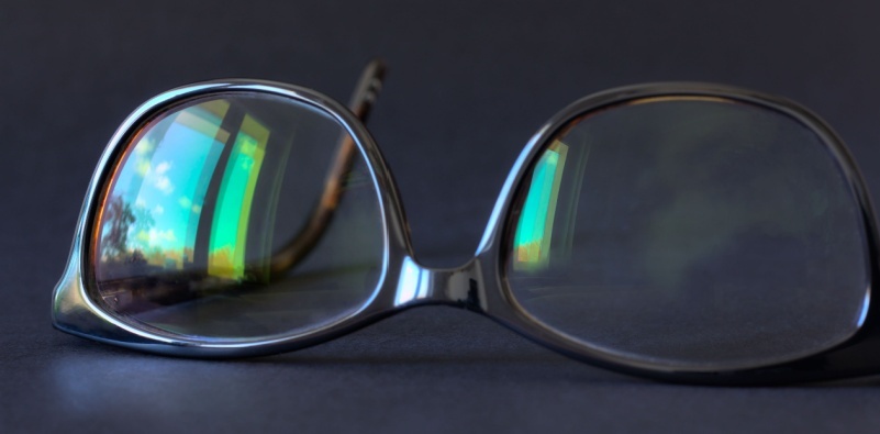 A pair of glasses on a surface, showing visible window reflections in the lenses