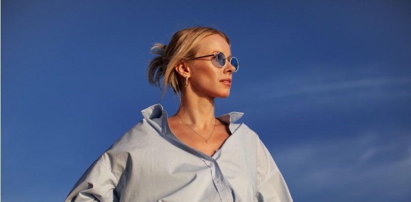 A blonde-haired woman wearing an oversized shirt and sunglasses stood outside