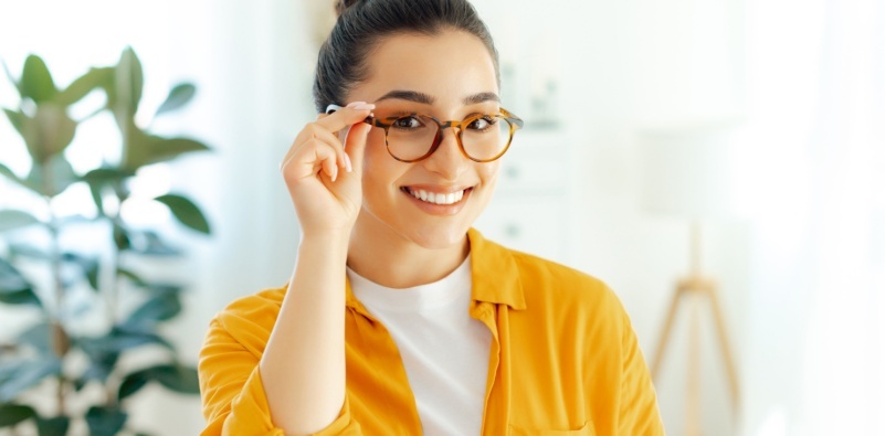 A young woman in a yellow shirt, holding on to the side of her glasses