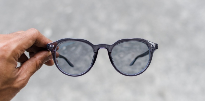 A man’s hand holding a pair of glasses with photochromic lenses.