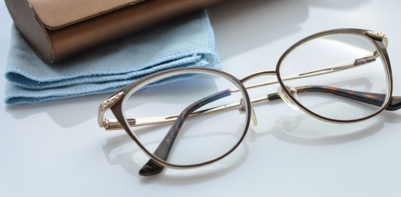 A pair of eyeglasses on the table with a glasses case and a cleaning cloth