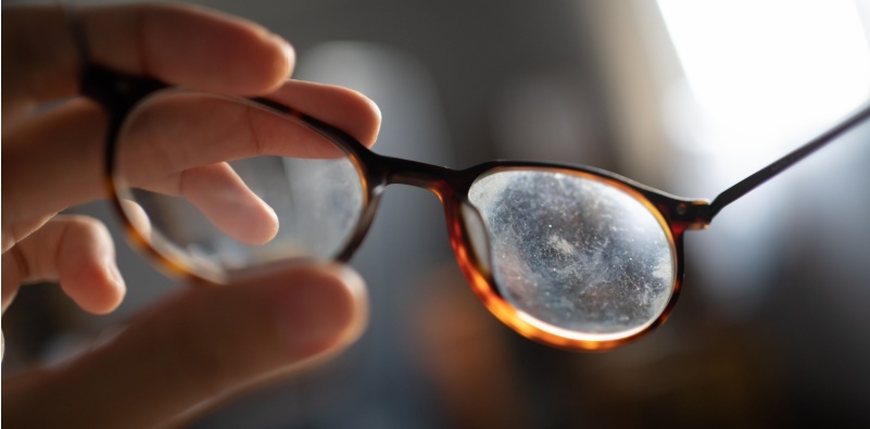 A person holding glasses with dirty and scratched lenses, highlighting the need for lens replacement