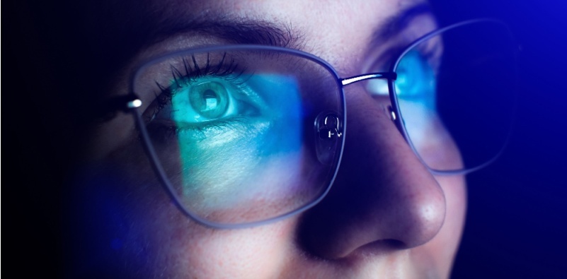 A close-up of a woman wearing glasses with blue light blocking coating, designed to reduce eye strain from prolonged screen exposure