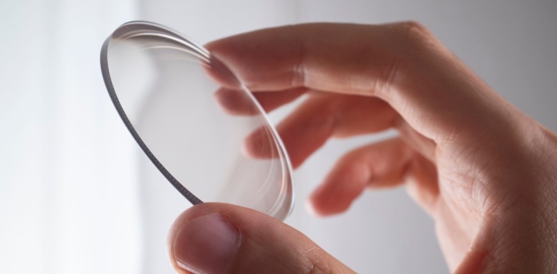 A close-up of a person holding an eyeglasses lens between their fingers.