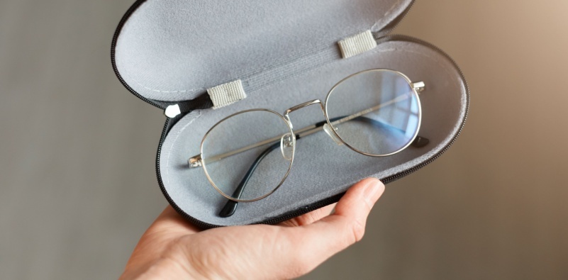 A person holding a pair of silver prescription glasses in a glasses case, showcasing stylish and protective storage