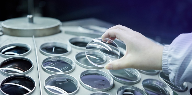 An image of an eyeglasses lens making lab with a person holding an unfinished spectacle lens.