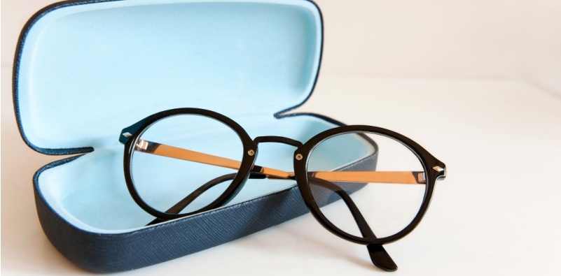 An open glasses case on a white surface with a pair of black, round eyeglasses half in and half out of the case.