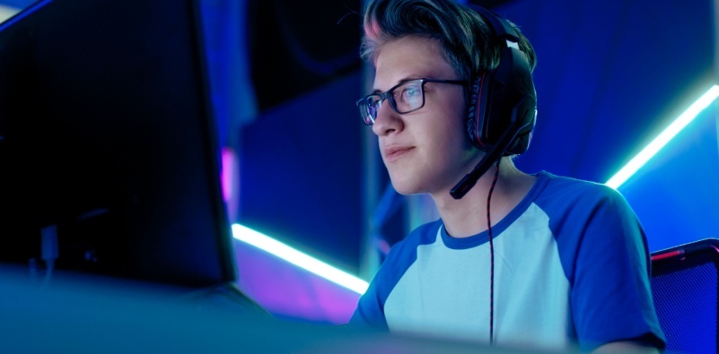 A teenage boy playing computer games, wearing blue light glasses to protect his eyes from screen glare and digital eye strain