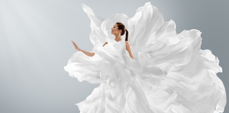 A woman in long silk gown with chiffon fabric flying on wind over light gray background