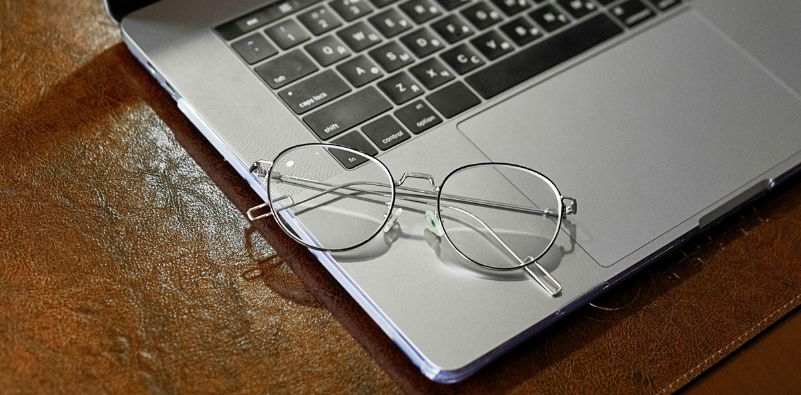 A pair of metal eyeglasses resting on a silver laptop by the keyboard