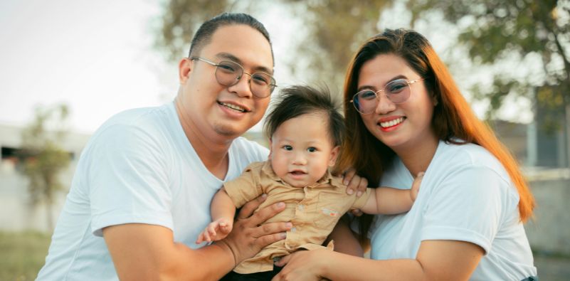 A family with a baby sat outside, wearing eyeglasses