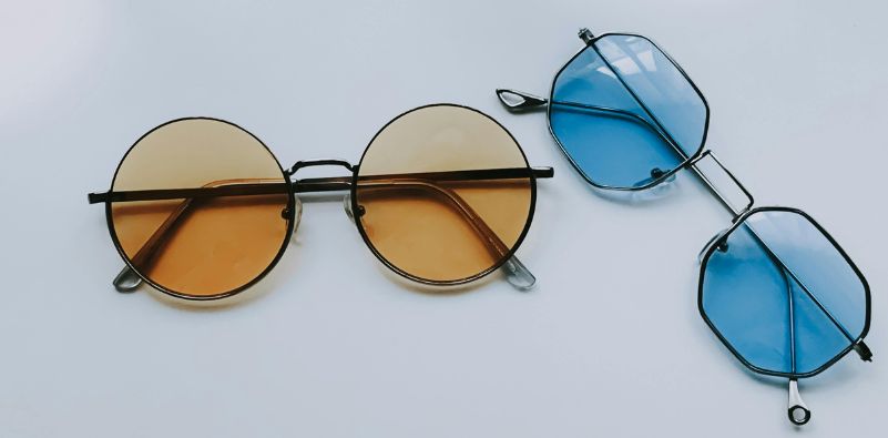 A pair of round eyeglasses with orange lenses and a pair of hexagonal eyeglasses with blue lenses on a white background
