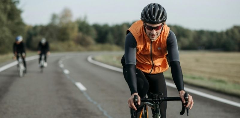 A man wearing an orange vest and cycling glasses on his bike.